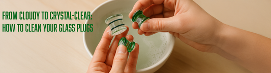 hands washing glass double flare plug jewelry in a bowl with soapy water on a light wood table