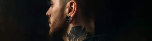 view of man from the side. he has a glass ear tunnel in his stretched earlobe. he has short grown hair, a light beard and moustache, and neck tattoos. he is cool and edgy
