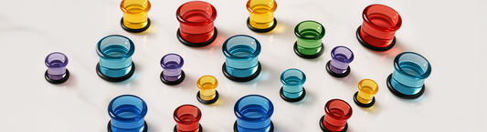 single flare various bright colored glass tunnel ear jewelry in different sizes on white marble ground